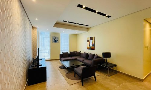 Luxury apartment living room with l-shaped sofa, decorative textured wall, artwork, and ceiling lighting.