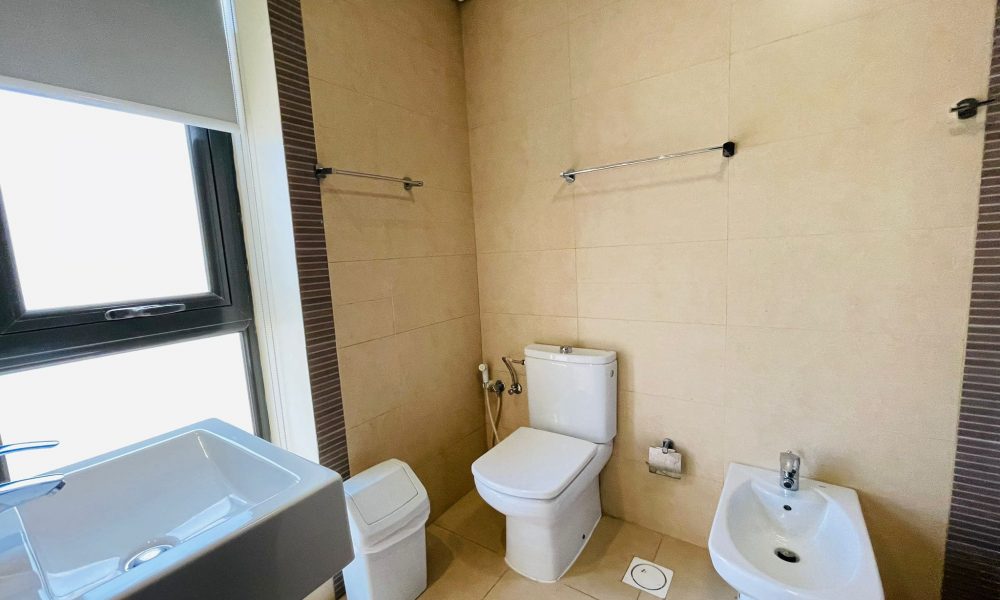 Luxury 2 BR apartment bathroom interior featuring a bathtub, toilet, bidet, and basin, with beige and stripe tiled walls.