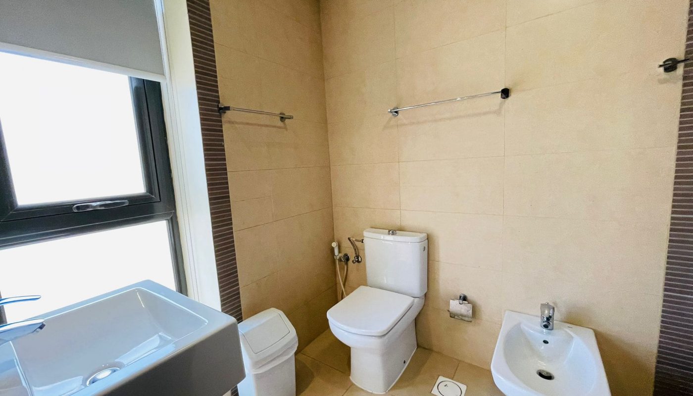 Luxury 2 BR apartment bathroom interior featuring a bathtub, toilet, bidet, and basin, with beige and stripe tiled walls.