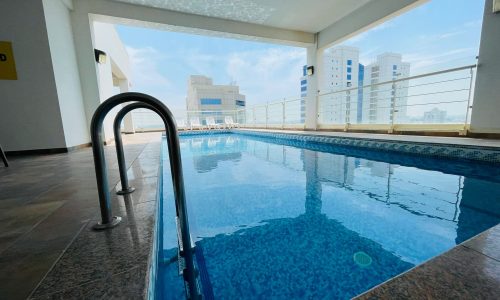 Luxury apartment with an indoor swimming pool, metal ladder, surrounded by glass walls and overlooking city buildings in Sanabis.