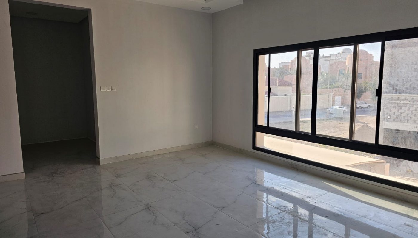 Empty room with white walls, marble floor, a large window on the right letting in daylight, and an open doorway on the left.