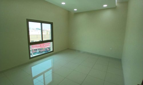 Empty room in a brand new apartment with white tiled floor, large window, and recessed ceiling lights.