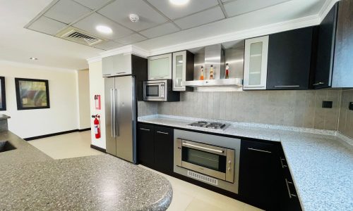 Luxury apartment kitchen interior in Juffair with dark cabinetry, built-in stainless steel appliances, and granite countertops. A fire extinguisher is visible near the refrigerator.