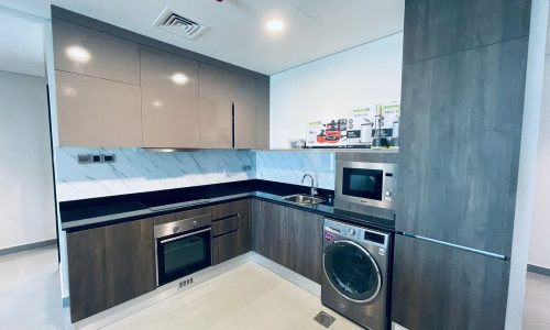 A modern kitchen with gray cabinetry, stainless steel appliances, a washing machine, and marble countertops.