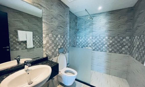 A modern bathroom with patterned stone walls, featuring a sink, mirror, toilet, and a glass shower enclosure.