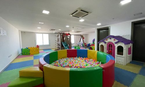 Colorful indoor children's playroom in a luxury 1 BR apartment in Juffair, featuring a ball pit, slide, and playhouses on a multi-colored floor mat.