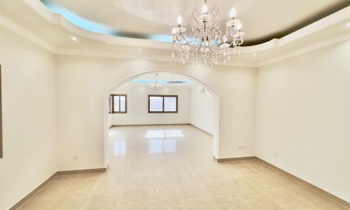 Empty, spacious, brightly lit room with tiled floors, white walls, arched doorways, and a crystal chandelier.