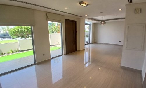 A spacious empty villa with shiny tiled flooring, large windows, and sliding glass doors leading to a garden.