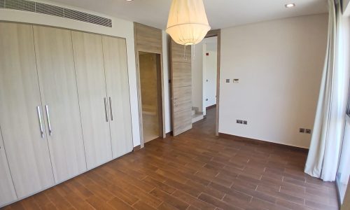 Empty modern villa with polished brown floor tiles, large wardrobe, and a hanging lamp. There's a curtain-covered window and a wooden door.