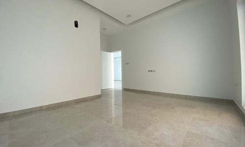 Empty, modern villa for sale with white walls, marble flooring, and recessed ceiling lights in Bani Jamra.