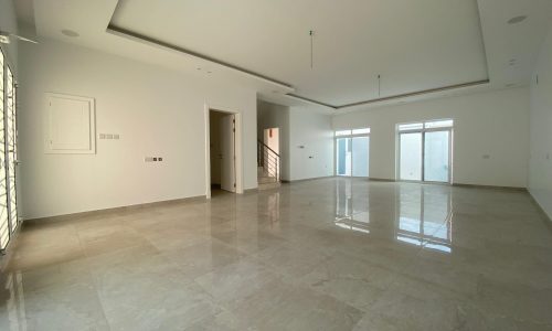 Empty, modern villa in Bani Jamra with polished marble floors and white walls, featuring multiple windows and recessed ceiling lights.