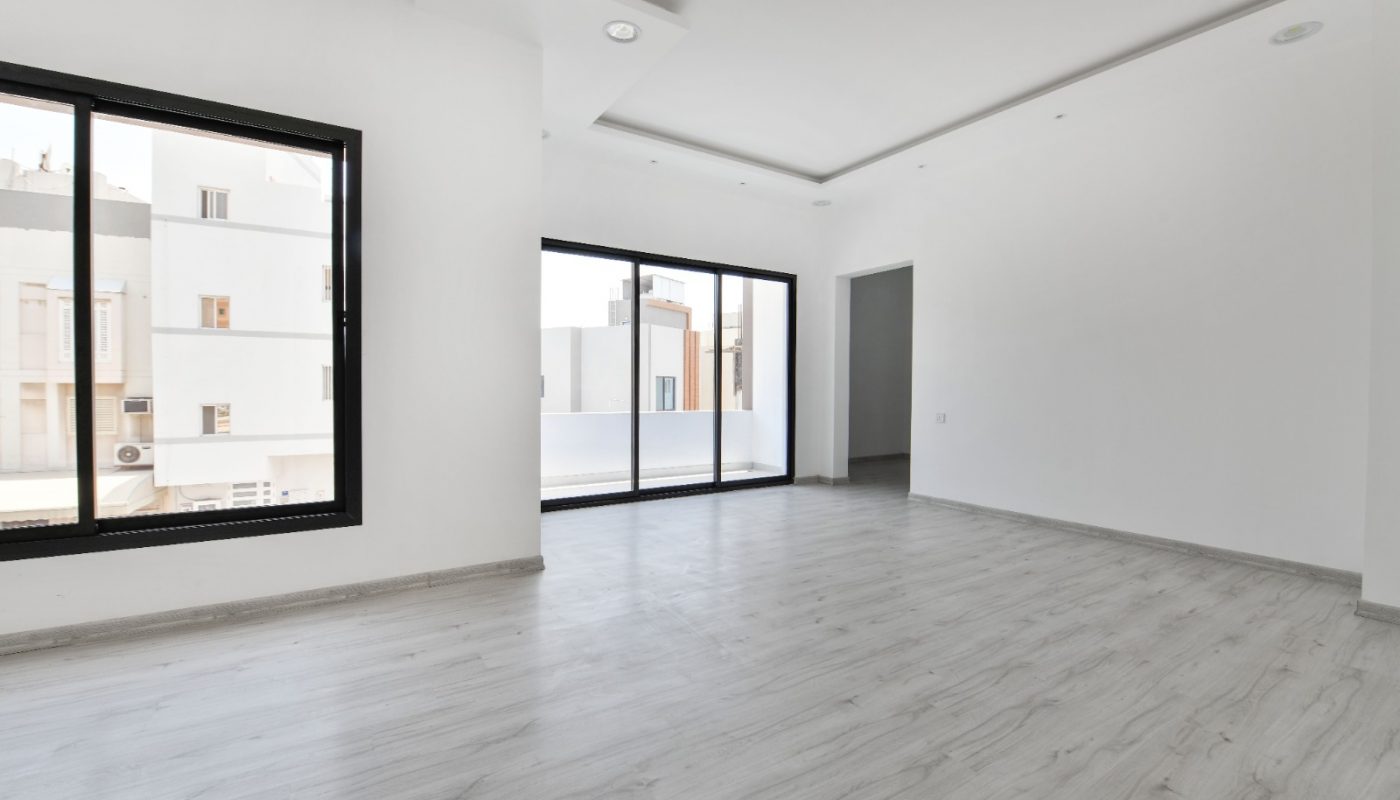 Unfurnished, modern, white-walled room with light wood flooring, large windows, and a sliding glass door leading to a balcony.