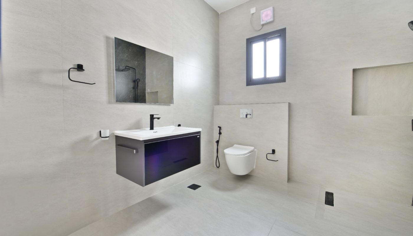 Minimalist bathroom with light beige walls and floor, floating vanity with sink, wall-mounted toilet, large mirror, window, and built-in shower niche.