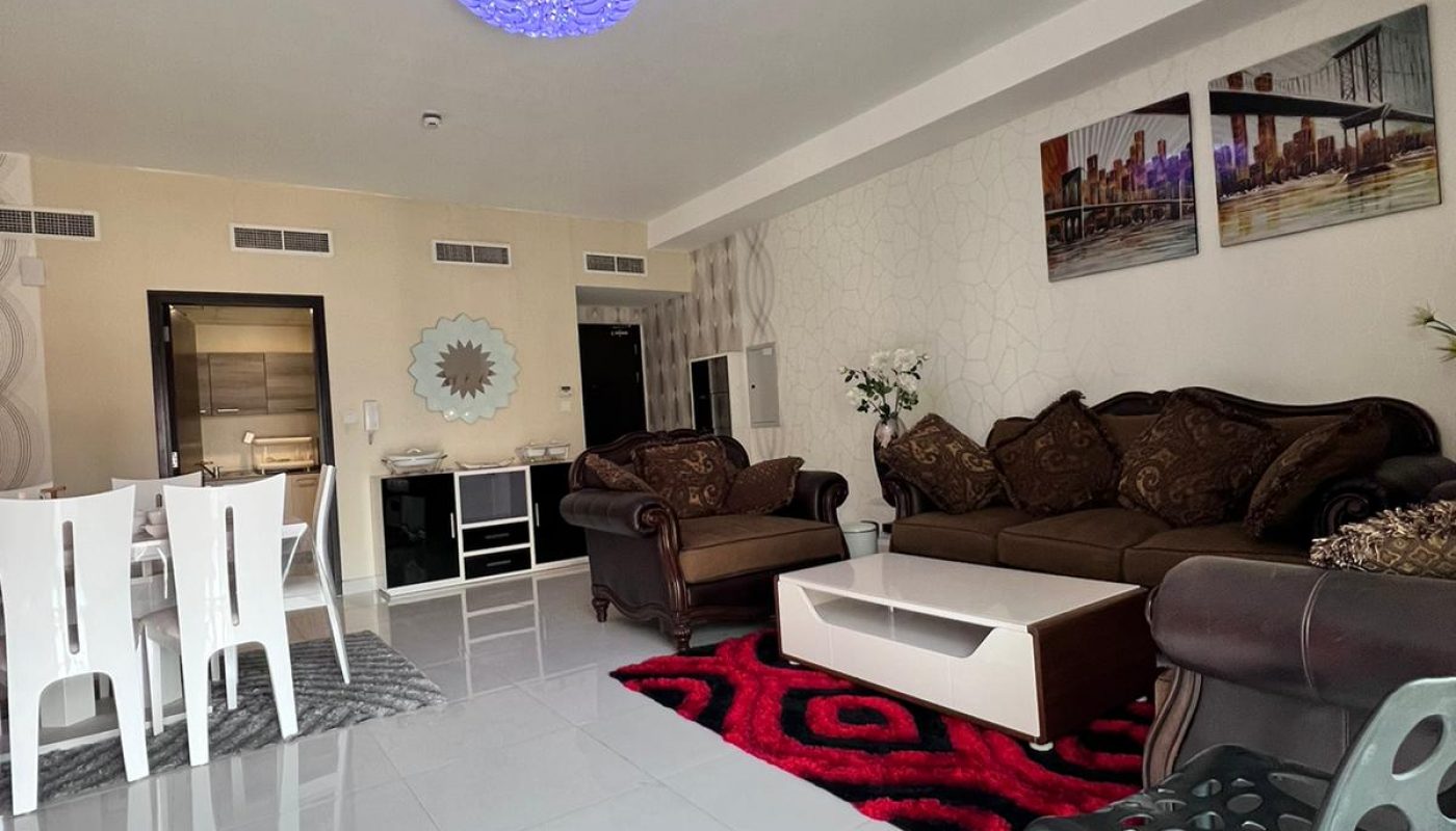 Modern living room with brown sofas, white dining table, black chairs, a patterned red rug, and wall art; bright lighting and glossy white tile flooring.