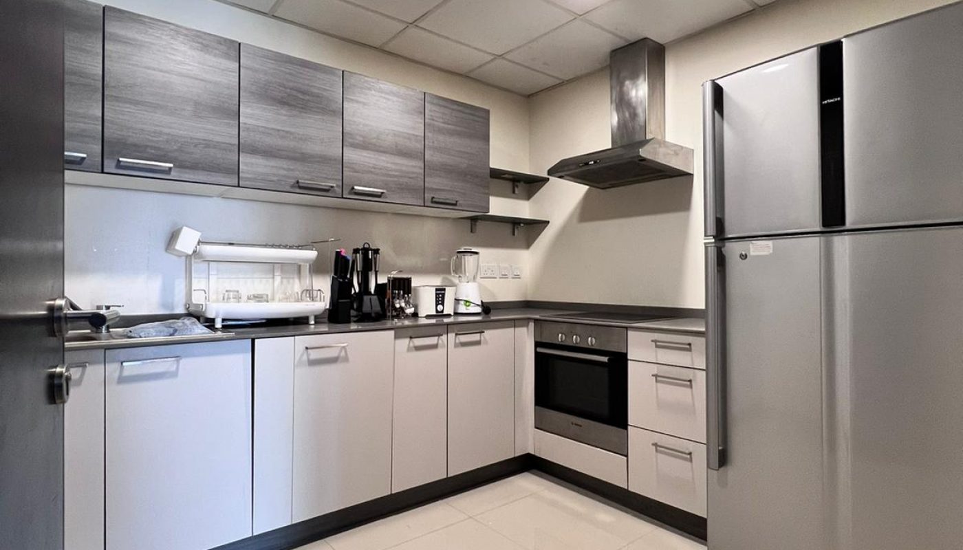 Modern kitchen with grey cabinets, stainless steel appliances, refrigerator, oven, stove, sink, and white tile floor under bright ceiling lights.