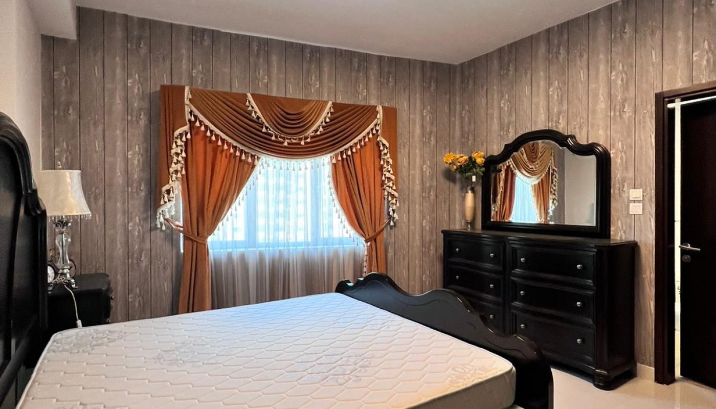 A bedroom features a dark bed frame, a dresser with a mirror, orange curtains over a window, and wood-patterned walls.