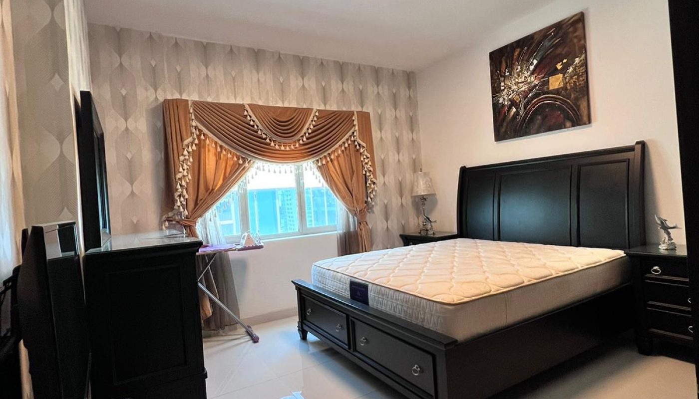 Bedroom with a large bed, TV on a dresser, nightstands, tiled floor, window with gold curtains, and wall art above the bed.