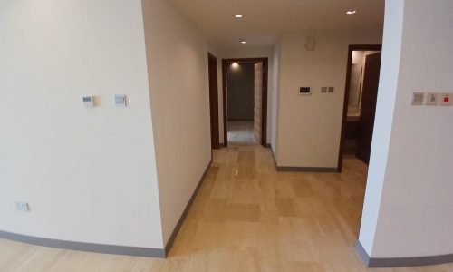 A hallway with tiled flooring and white walls leads to multiple open doorways. Light switches and thermostat controls adorn the walls. This spacious flat for sale offers modern living in the heart of Dilmunia Island.