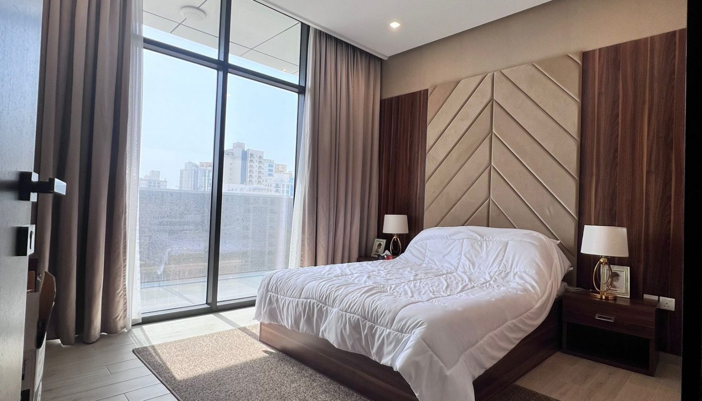 Modern bedroom with a large bed, wood accents, nightstands with lamps, floor-to-ceiling windows, and a city view.