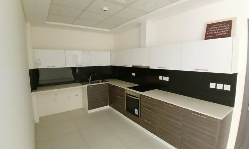 Modern kitchen with white upper cabinets, dark lower cabinets, white countertops, black backsplash, built-in stove, oven, and sink. Ceiling has recessed lighting and ventilation. Wall-mounted plaque displayed.