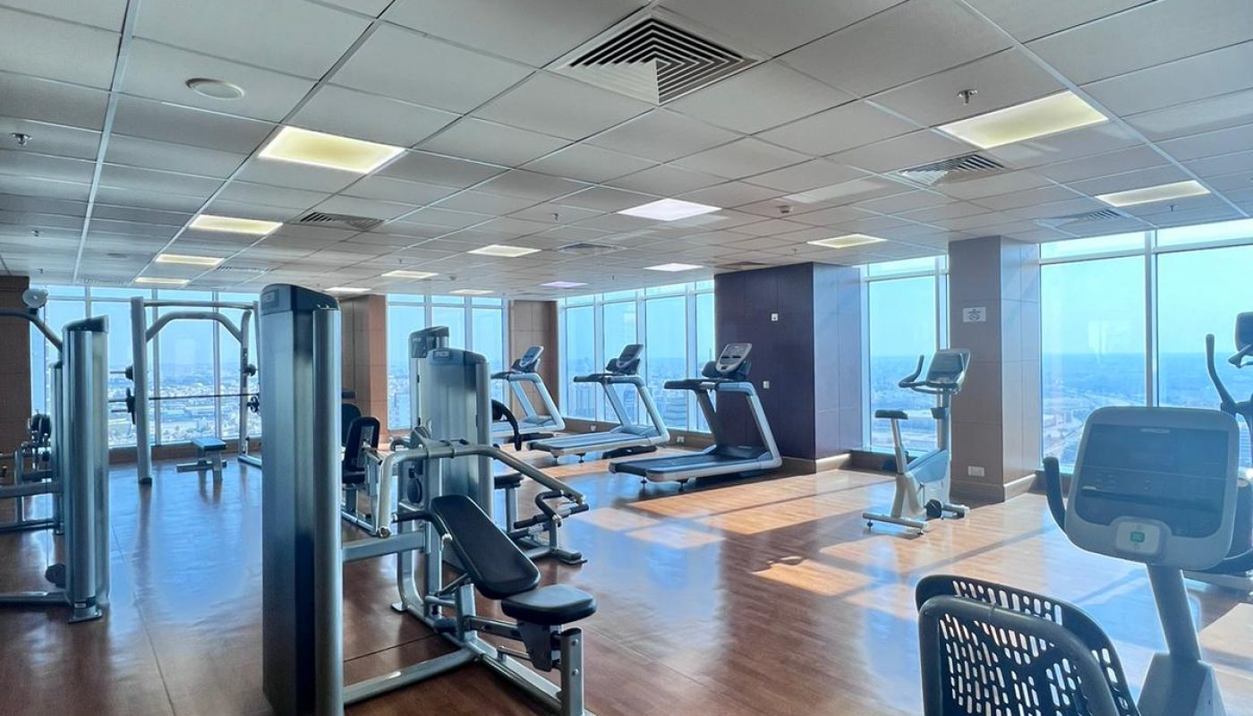 Spacious gym with wooden floors, large windows, and various exercise machines including treadmills, stationary bikes, and weight equipment.