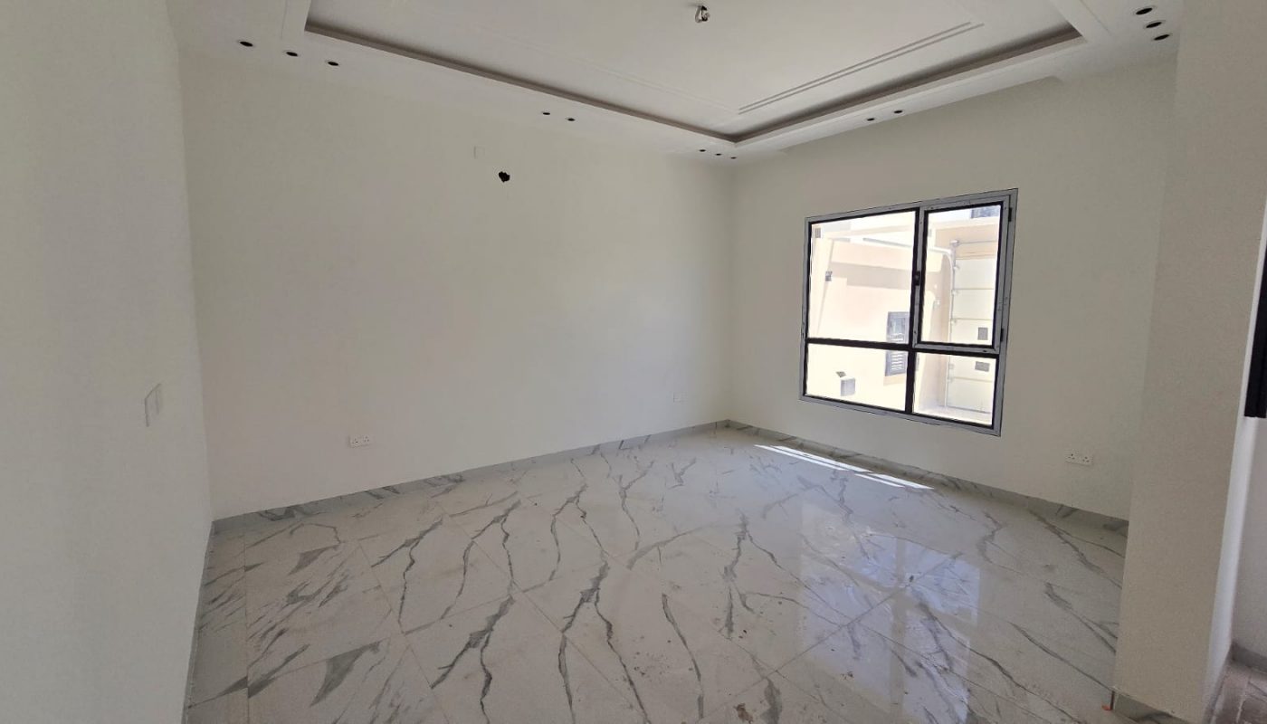 Empty room with white walls, a large window, and marble tile flooring. The ceiling features recessed lighting spaces without fixtures installed. Sunlight enters through the window. Ideal for new villas in Damistan, this space is now for sale.