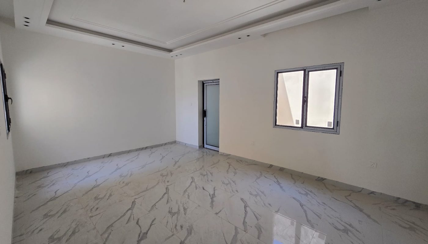A vacant, well-lit room with white walls, a window, a door, and glossy white marble floor tiles in the desirable Damistan area. New villas for sale nearby offer modern amenities and stunning finishes.