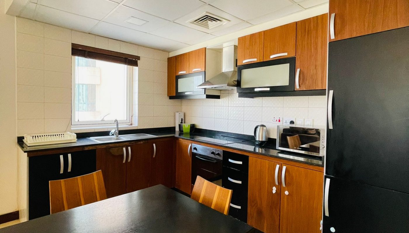 Modern kitchen with wooden cabinets, black countertops, a dining table with four chairs, and various appliances including a microwave, oven, toaster, and kettle.