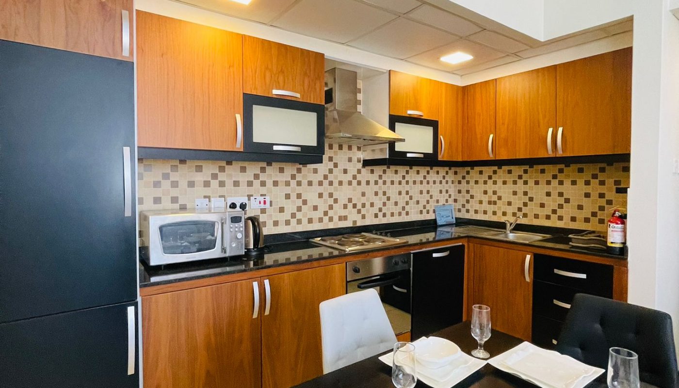 Modern kitchen with wood cabinets, black appliances, a tiled backsplash, and a set dining table with four plates and glasses.