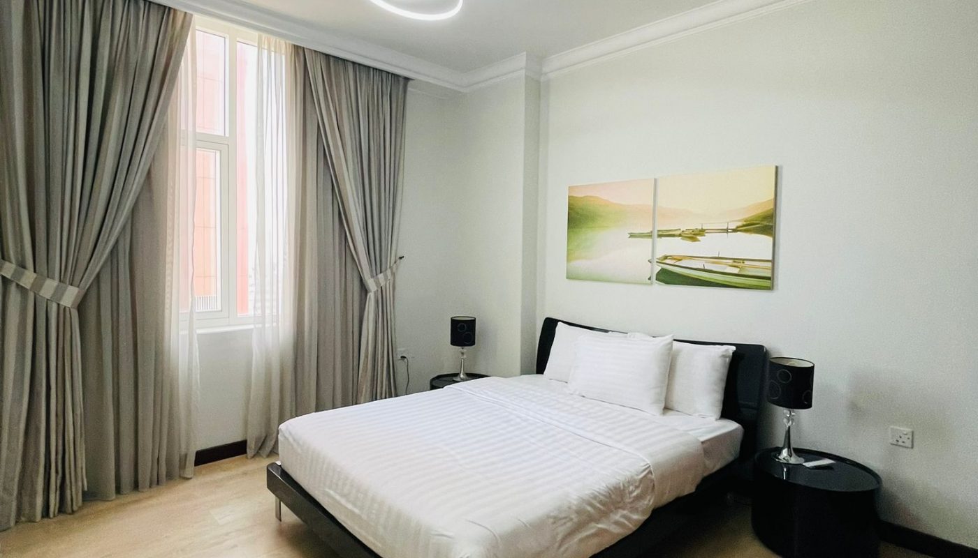 A modern, minimal bedroom with a double bed, white bedding, two nightstands, a large window with curtains, light wood flooring, and a landscape painting above the bed.