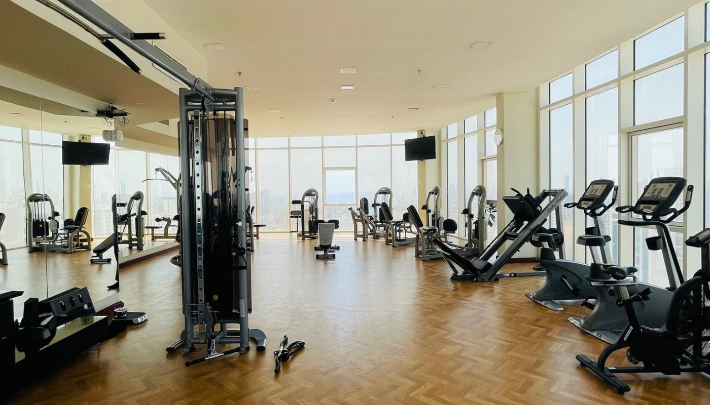 Spacious gym with wooden flooring, large windows, and various exercise machines including treadmills, ellipticals, and strength training equipment.