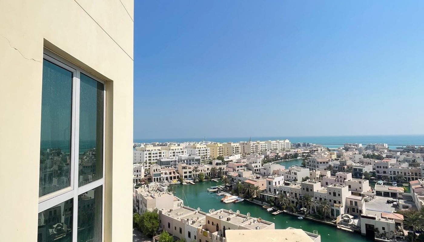 View from a balcony showing a residential area with waterways, several buildings, and a clear blue sky in the background.