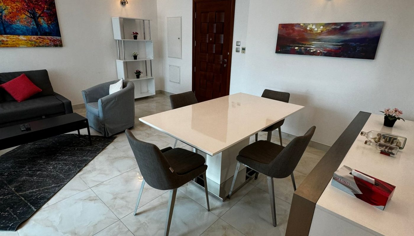 Modern living and dining area with a white table, four gray chairs, a sofa, wall art, and tiled floors.