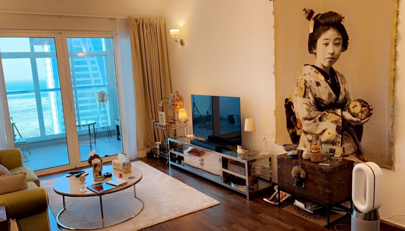 Living room with a large wall art of a woman in traditional attire, a TV on a console, a round coffee table, and floor-to-ceiling windows with a view of high-rise buildings.