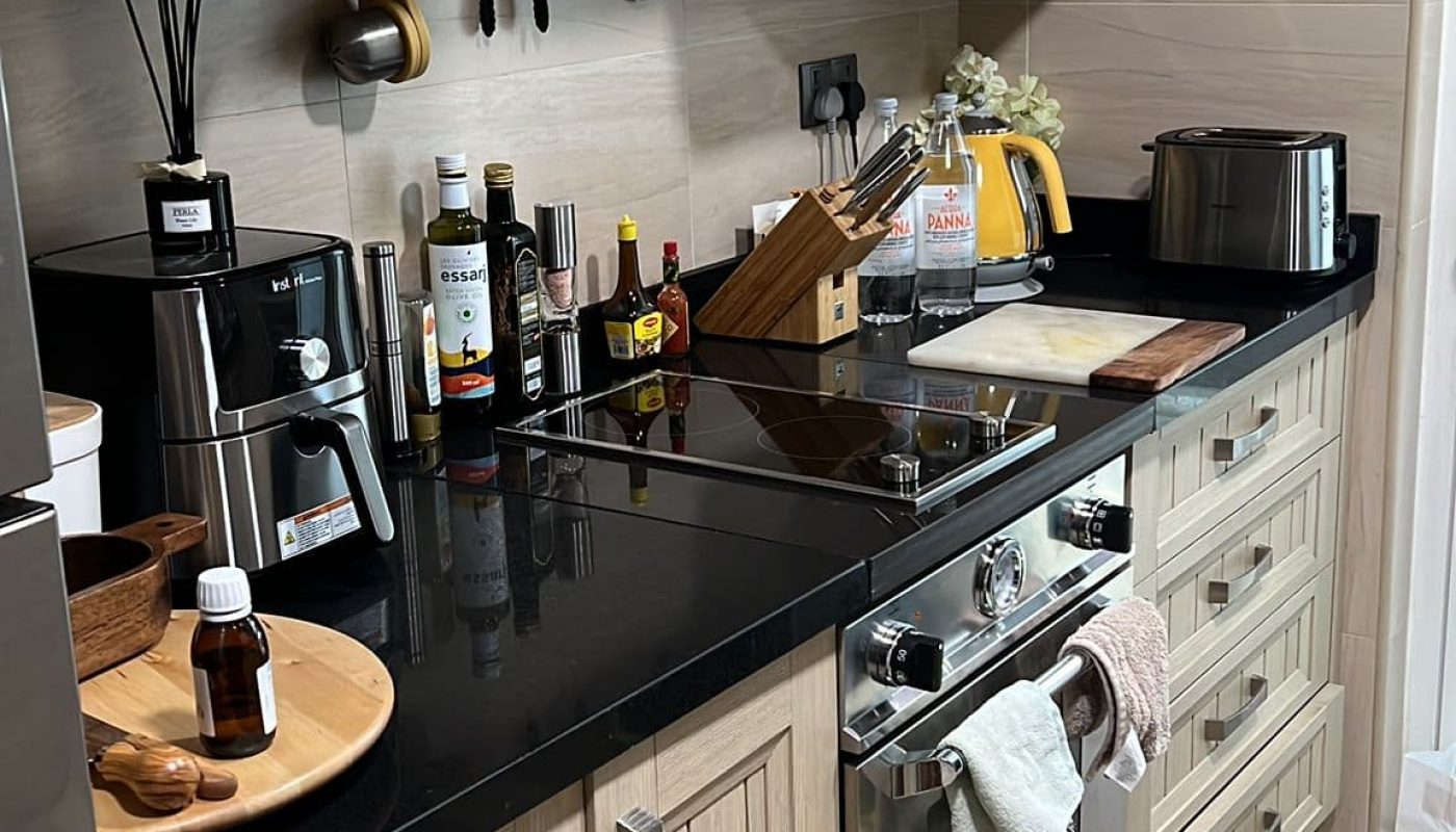 A kitchen with wooden cabinets, black countertop, oven, toaster, and various kitchen appliances and bottles. A towel hangs on the oven handle.