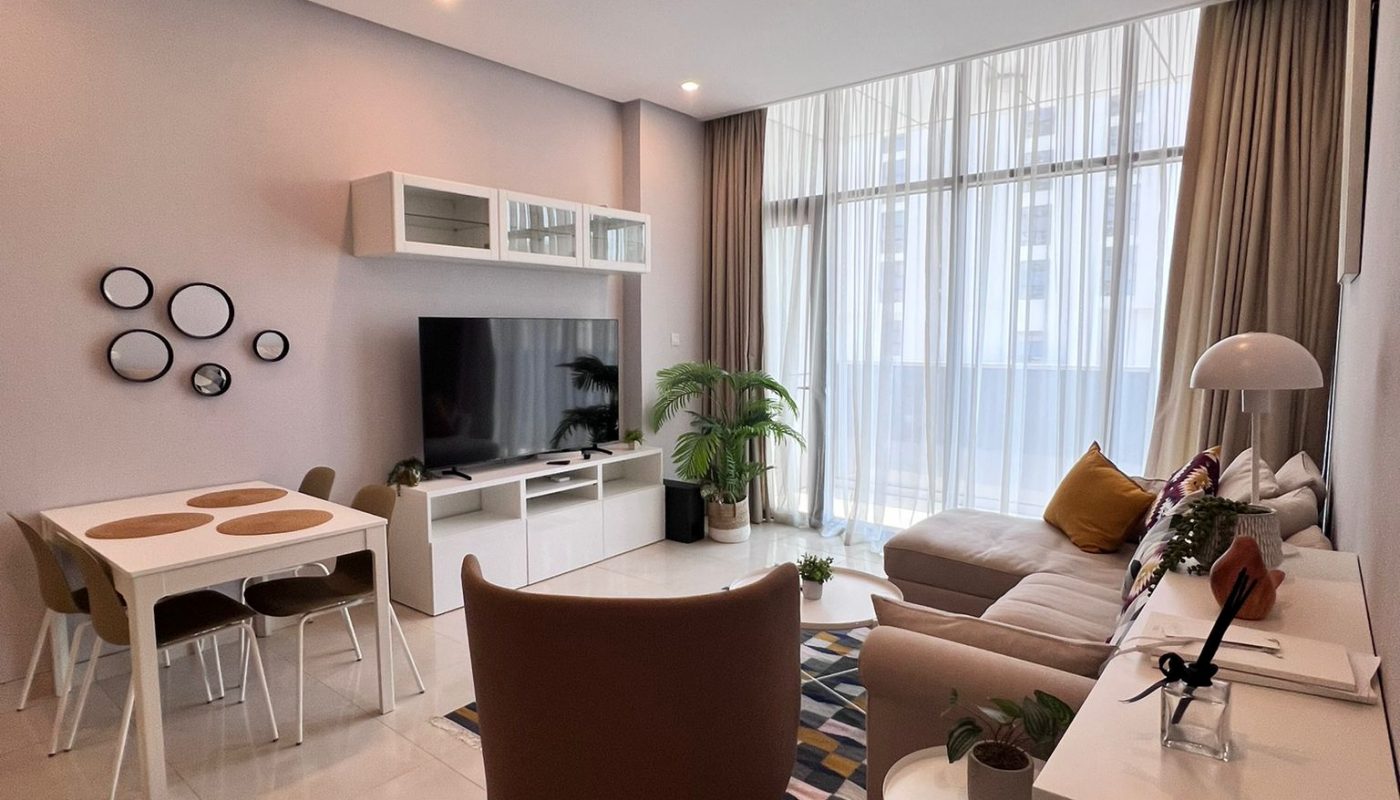 Modern living room with a sofa, TV, dining table, armchairs, potted plants, and large window with sheer curtains, decorated in neutral tones.