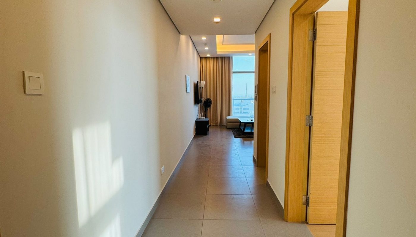 A long hallway with tiled floors leads to a bright living area with floor-to-ceiling windows.