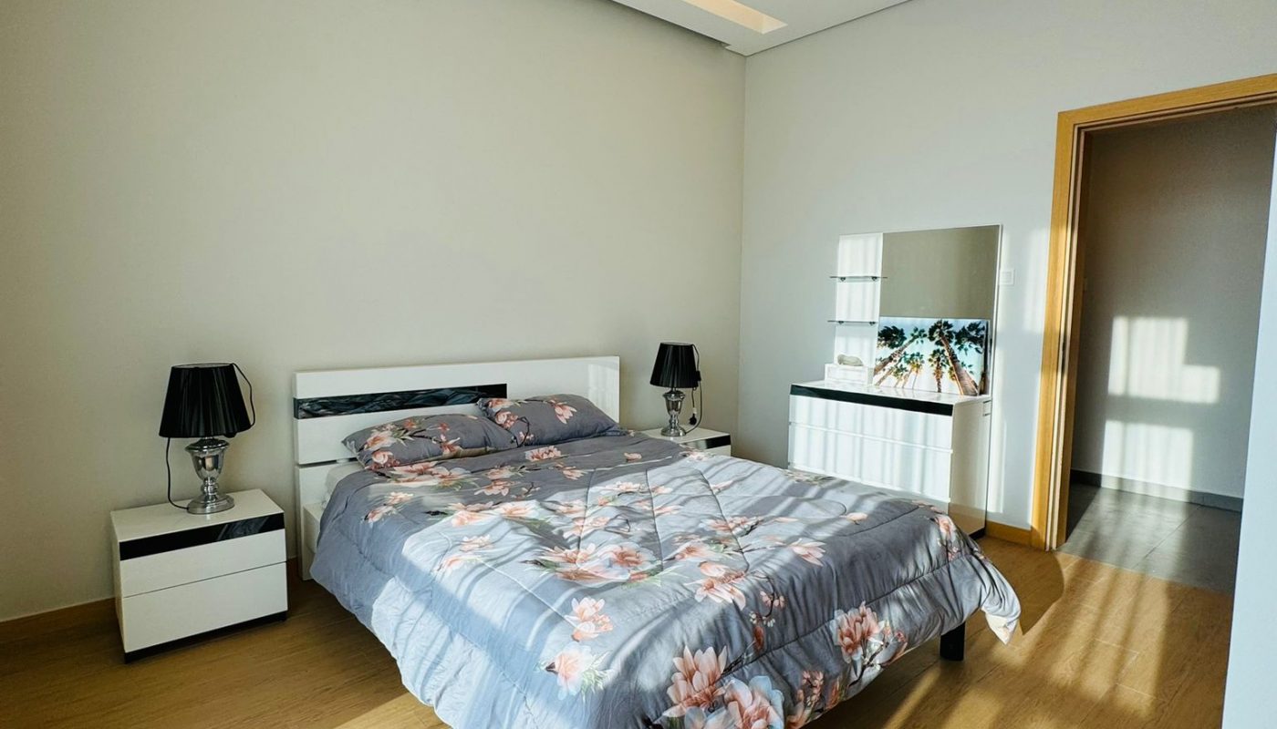A modern bedroom with a floral-patterned grey bedspread, two nightstands with black lamps, and a dresser with a mirror.
