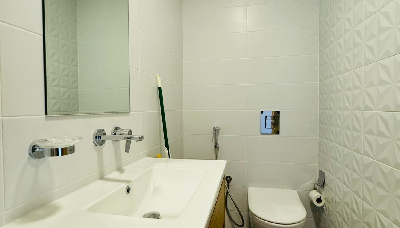 A small, modern bathroom with a white vanity sink, a wall-mounted toilet, and white tiled walls.