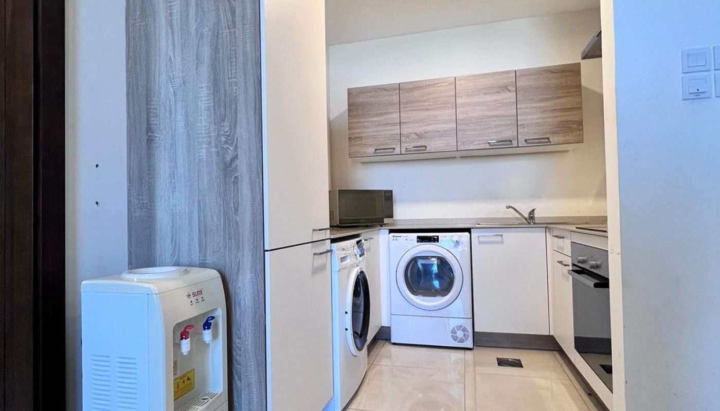 Modern kitchen with light tile floor, washing machine, dishwasher, oven, sink, upper and lower cabinets, and a water dispenser in the foreground near a refrigerator.