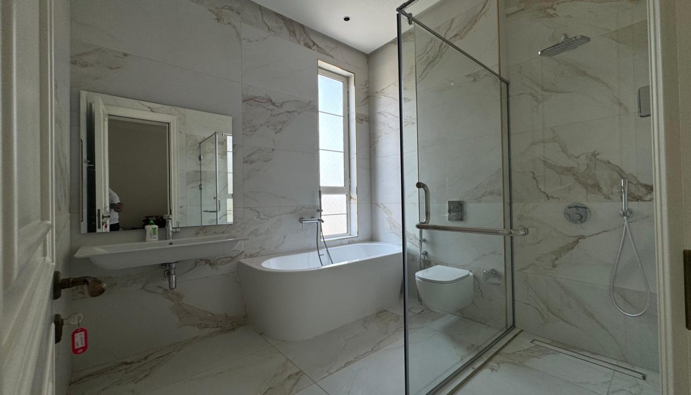 Modern bathroom with gray marble tiles, featuring a bathtub, glass-enclosed shower, toilet, sink with a mirror, and a window for natural light.