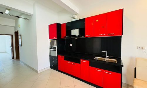 Modern kitchen with sleek red and black cabinets, a stainless steel oven, and a double sink on a tiled floor.