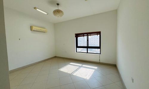 A vacant room with tiled floors, a window with blinds, an air conditioning unit, and overhead lights.