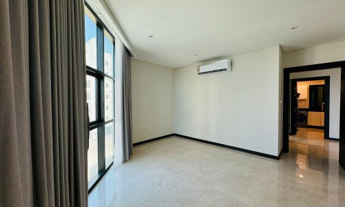 A bright, empty room with large windows, light-colored marble floors, gray curtains, and a wall-mounted air conditioning unit. A doorway leads to another area.