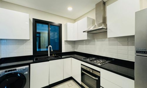 Modern kitchen with white cabinets, black countertops, a window, washing machine, gas stove, oven, and stainless steel range hood.