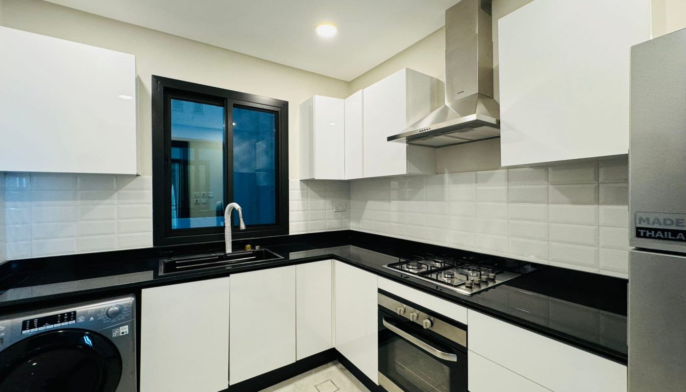 Modern kitchen with white cabinets, black countertops, a window, washing machine, gas stove, oven, and stainless steel range hood.