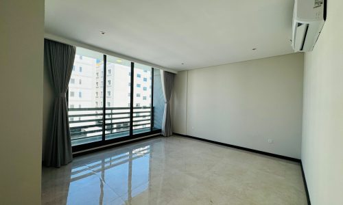 An empty room with a tiled floor, large windows with gray curtains, white walls, and a wall-mounted air conditioner.