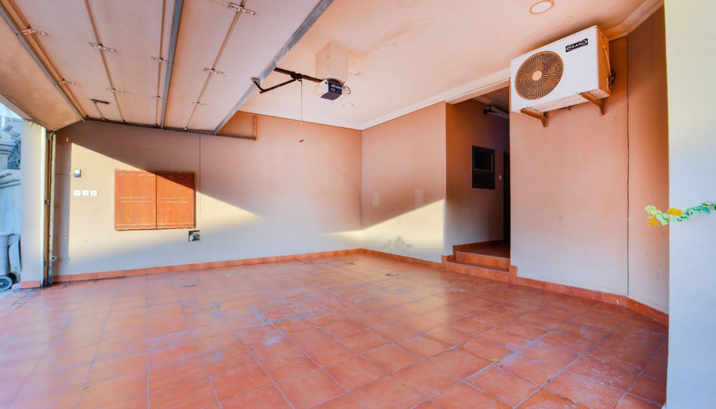 Empty garage with a tiled floor, beige walls, and an overhead door. An air conditioning unit is mounted on the wall.