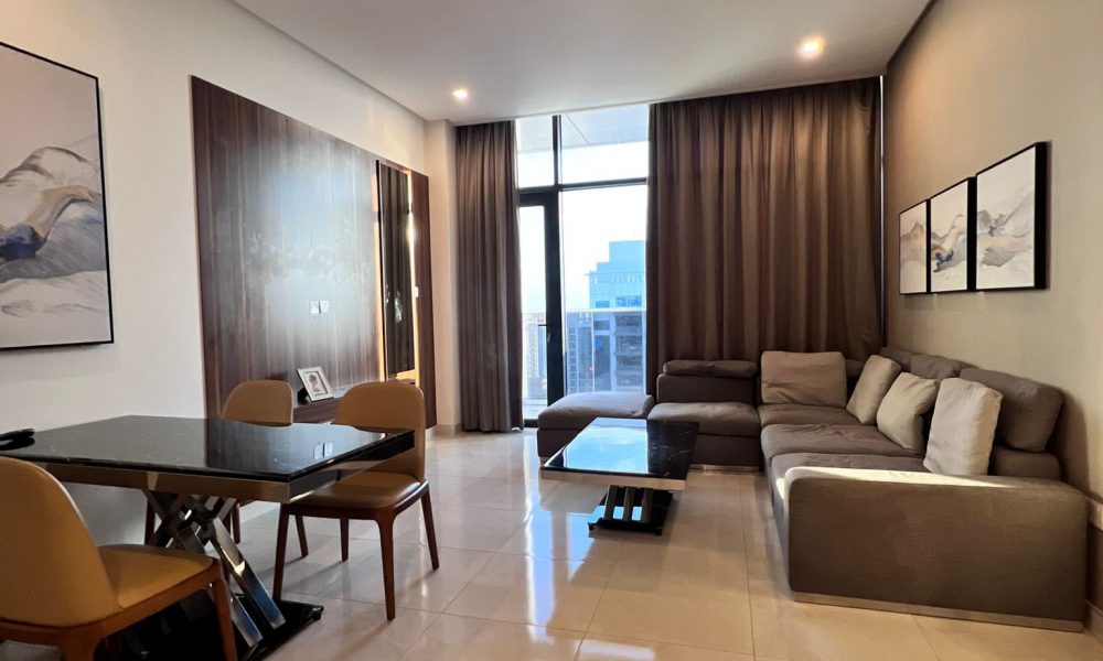 Modern living room with tiled floor, gray sectional sofa, two landscape paintings on the wall, dining area with table and chairs, large window with city view, and brown curtains.