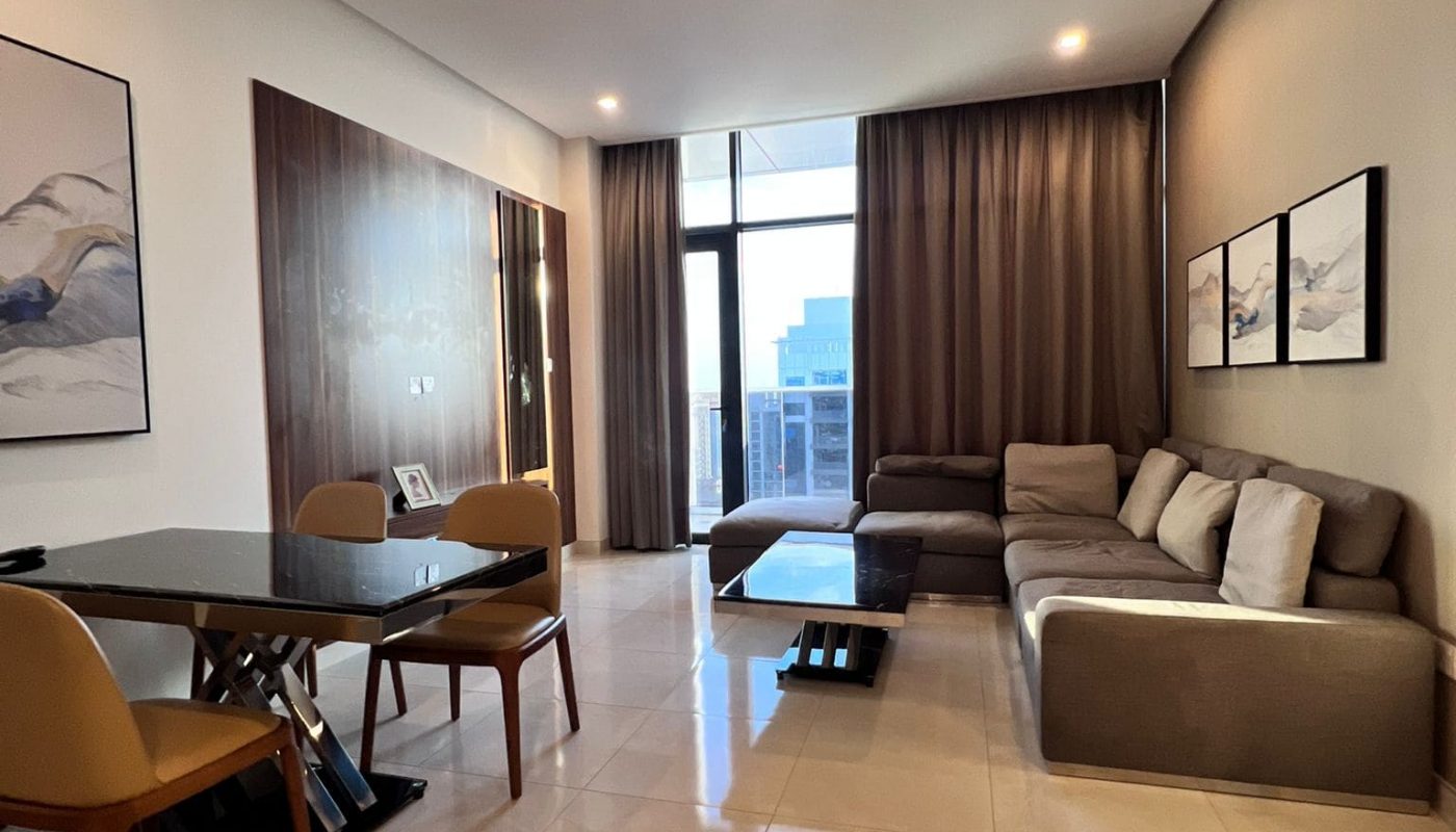 Modern living room with tiled floor, gray sectional sofa, two landscape paintings on the wall, dining area with table and chairs, large window with city view, and brown curtains.